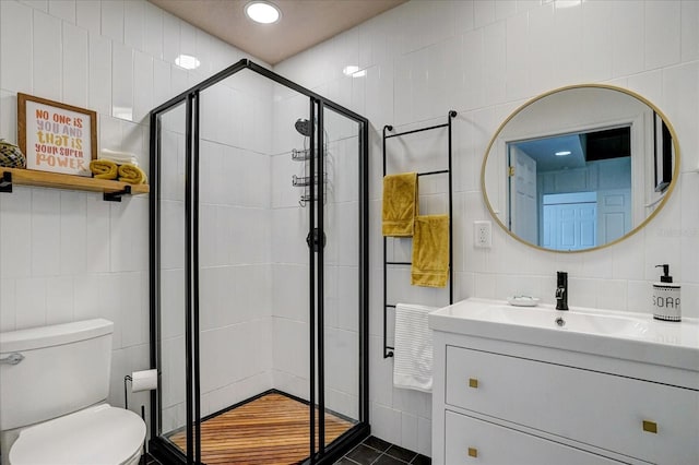 bathroom with vanity, tile walls, toilet, and a shower with door