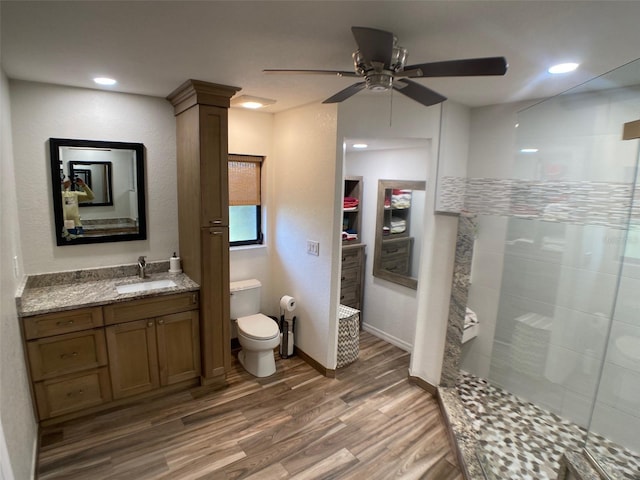 bathroom featuring toilet, wood-type flooring, tiled shower, vanity, and ceiling fan