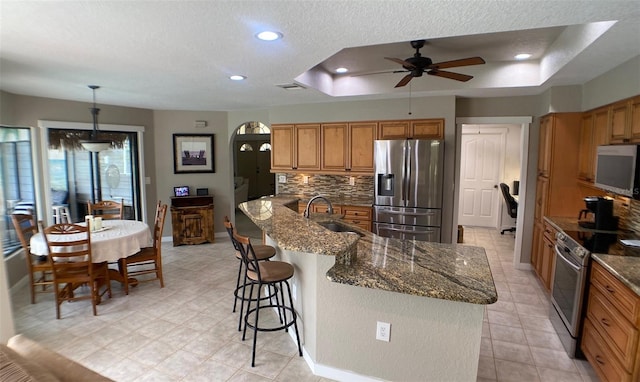 kitchen with hanging light fixtures, stainless steel appliances, a raised ceiling, a breakfast bar area, and sink