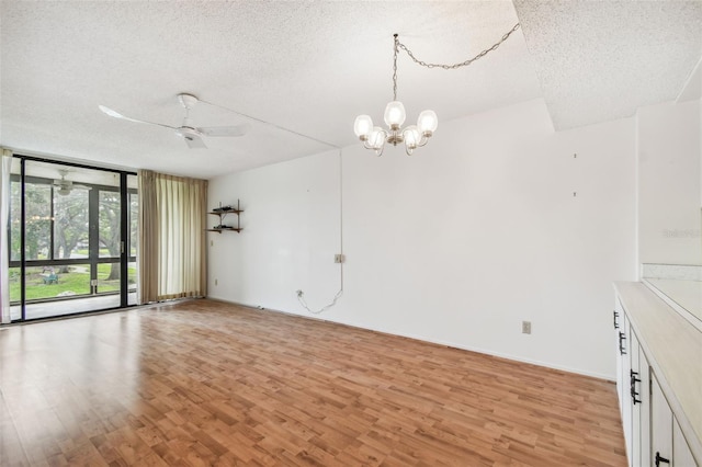 unfurnished living room featuring ceiling fan with notable chandelier, light hardwood / wood-style flooring, a wall of windows, and a textured ceiling