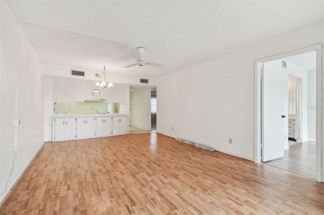 unfurnished living room featuring a textured ceiling, ceiling fan with notable chandelier, and light hardwood / wood-style flooring