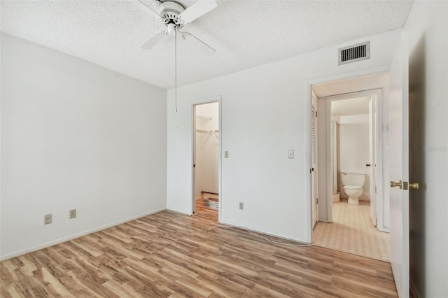 unfurnished bedroom with a textured ceiling, ceiling fan, a closet, light hardwood / wood-style flooring, and a walk in closet