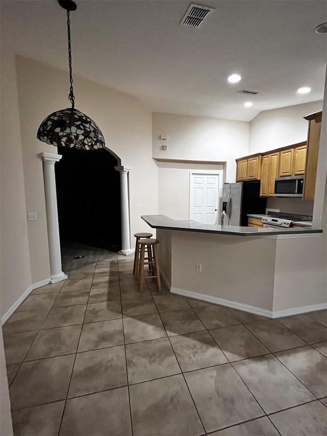 kitchen with kitchen peninsula, a kitchen bar, appliances with stainless steel finishes, decorative light fixtures, and ornate columns