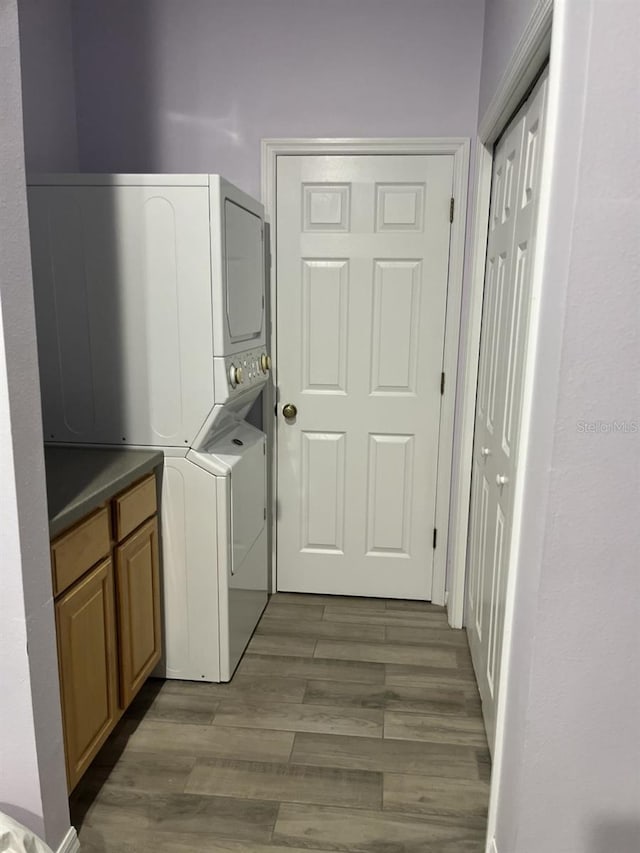 clothes washing area with stacked washer and clothes dryer, cabinets, and dark hardwood / wood-style flooring