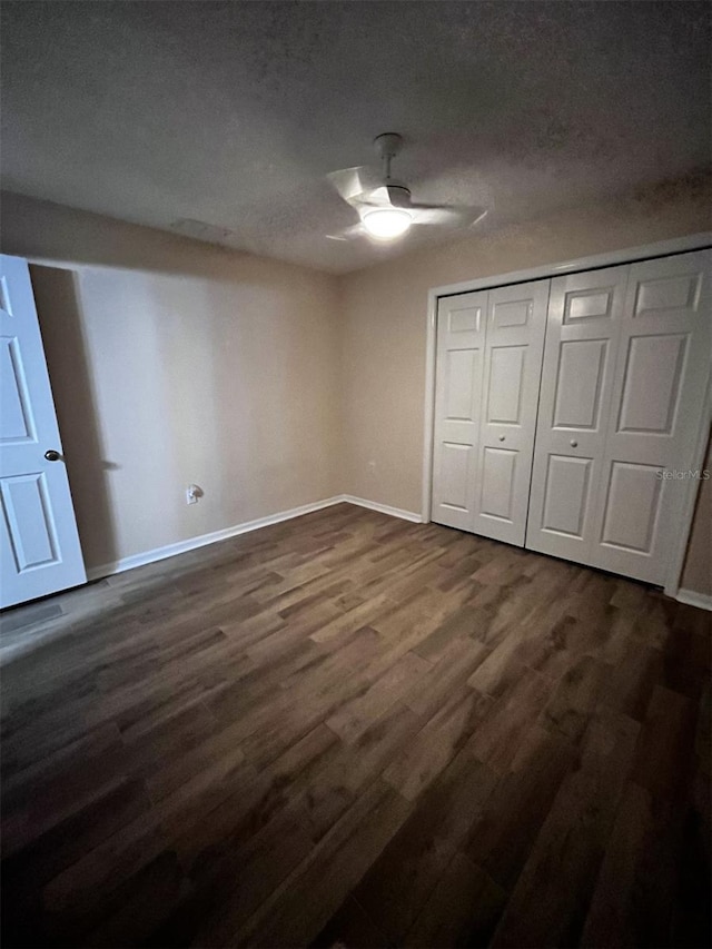 unfurnished bedroom with ceiling fan, a textured ceiling, a closet, and dark hardwood / wood-style floors