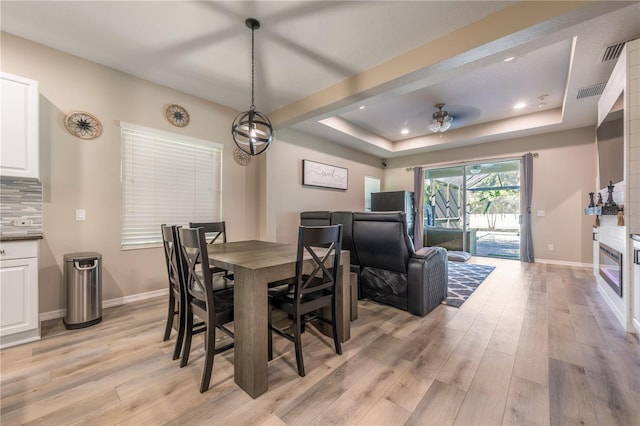 dining space with light wood-type flooring, a tray ceiling, and ceiling fan