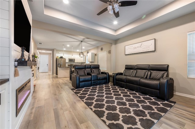 living room with ceiling fan, a raised ceiling, and light hardwood / wood-style floors