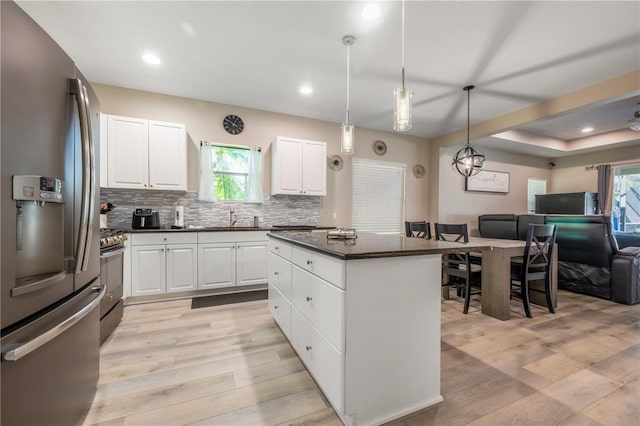 kitchen featuring appliances with stainless steel finishes, hanging light fixtures, light hardwood / wood-style floors, white cabinets, and a center island