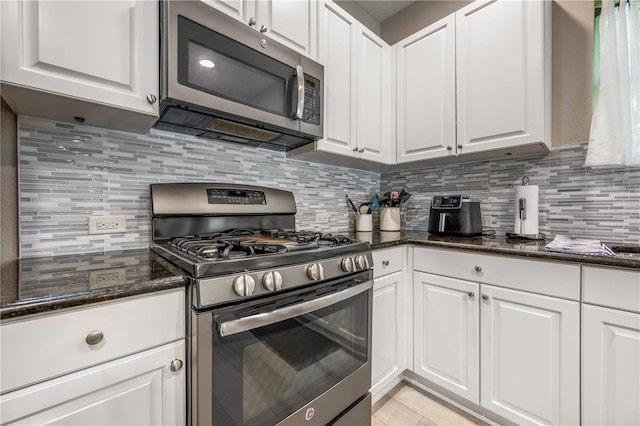 kitchen featuring dark stone counters, stainless steel appliances, white cabinetry, and tasteful backsplash