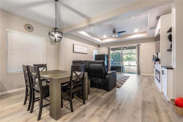 dining room with light hardwood / wood-style floors, a tray ceiling, and ceiling fan