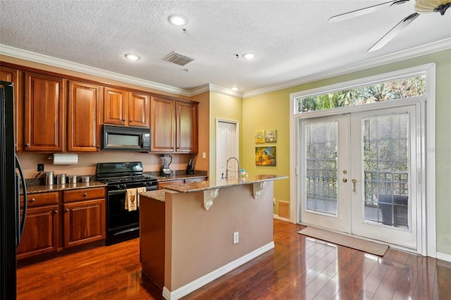 kitchen with a breakfast bar area, light stone countertops, black appliances, ornamental molding, and a center island with sink