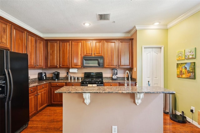 kitchen featuring a breakfast bar, dark stone countertops, a kitchen island with sink, black appliances, and dark wood-type flooring