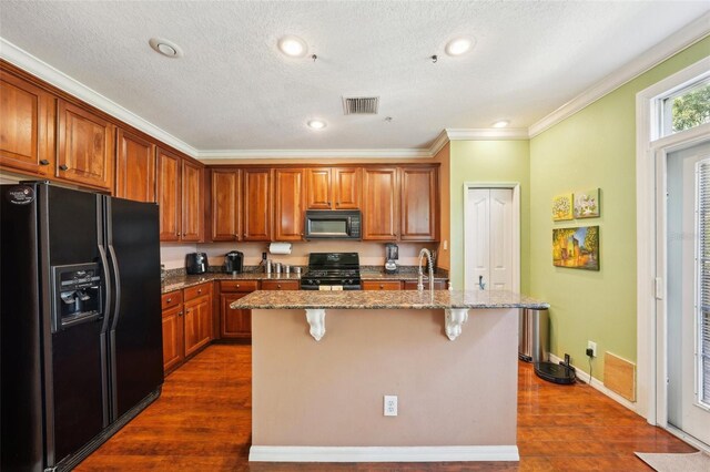 kitchen featuring a kitchen bar, stone countertops, dark hardwood / wood-style floors, an island with sink, and black appliances