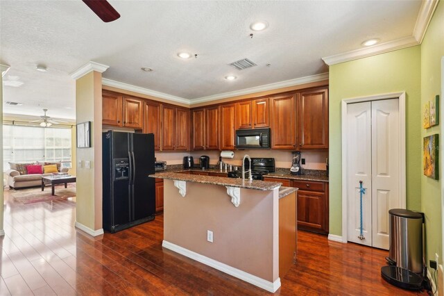 kitchen with dark wood-type flooring, ceiling fan, a kitchen island with sink, a kitchen breakfast bar, and black appliances