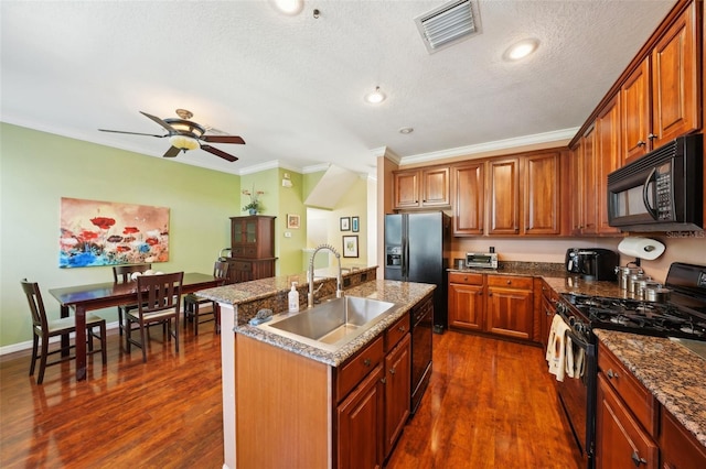 kitchen with sink, crown molding, dark wood-type flooring, black appliances, and an island with sink