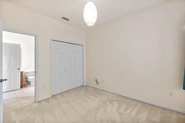 unfurnished bedroom with a closet, connected bathroom, and light colored carpet