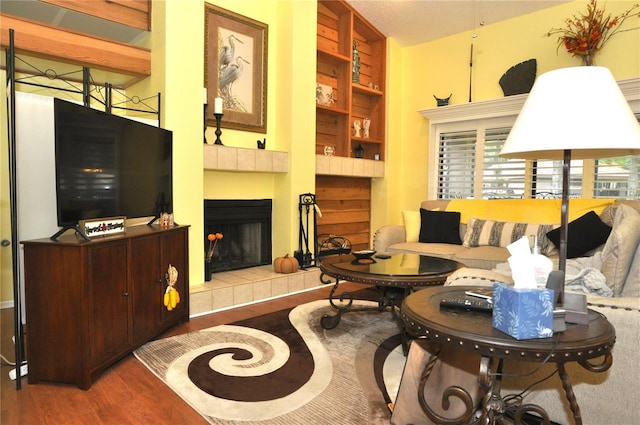 living room featuring vaulted ceiling, a fireplace, a textured ceiling, wood-type flooring, and built in shelves