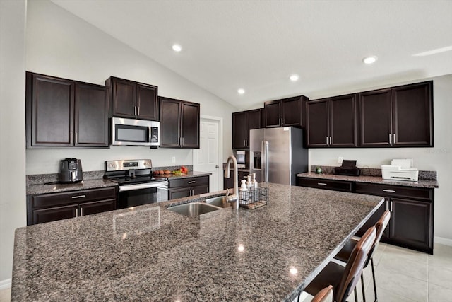 kitchen featuring an island with sink, sink, appliances with stainless steel finishes, a breakfast bar, and vaulted ceiling