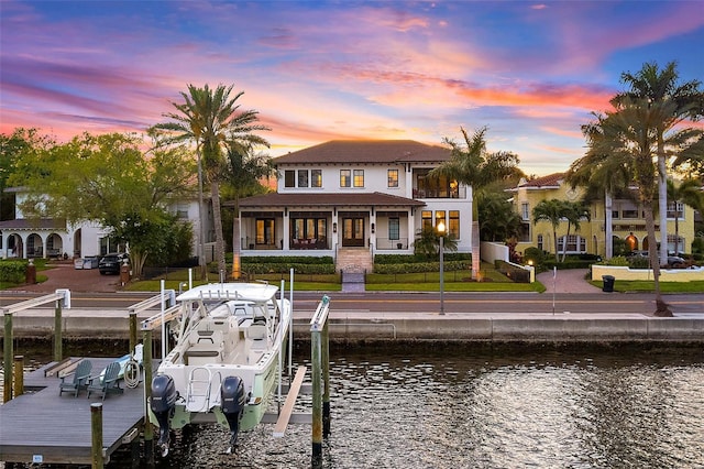 back house at dusk featuring a balcony, a lawn, and a water view