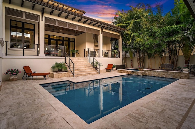 pool at dusk with an in ground hot tub and a patio area