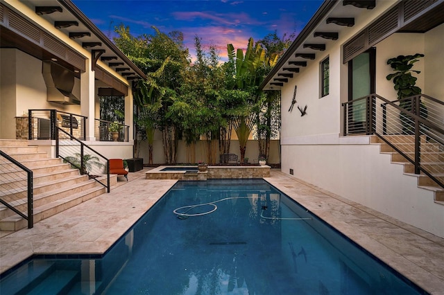 pool at dusk with an in ground hot tub and a patio area