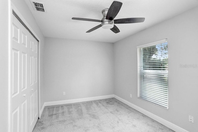 unfurnished bedroom with a closet, light colored carpet, and ceiling fan