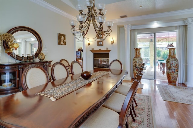 dining room with a notable chandelier, ornamental molding, light hardwood / wood-style floors, and ornate columns