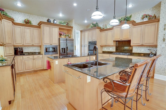 kitchen featuring sink, light brown cabinetry, an island with sink, and hanging light fixtures