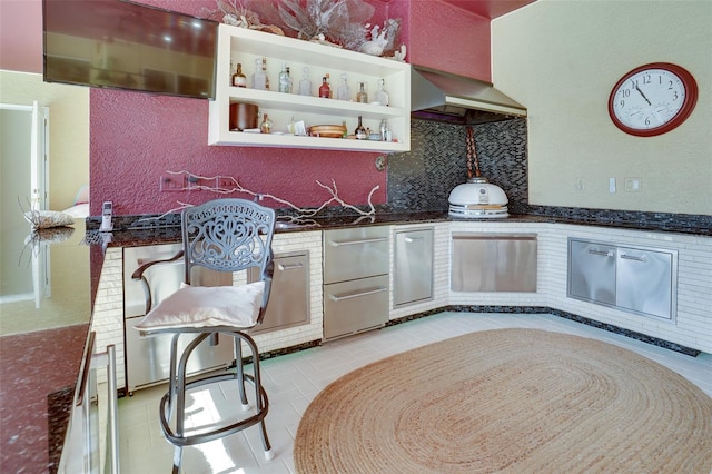 kitchen with backsplash, light tile patterned floors, dark stone counters, and wall chimney exhaust hood