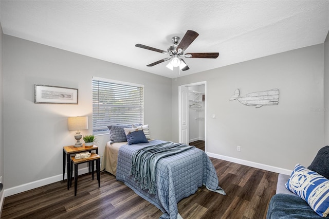 bedroom featuring a closet, dark wood-type flooring, a walk in closet, a textured ceiling, and ceiling fan