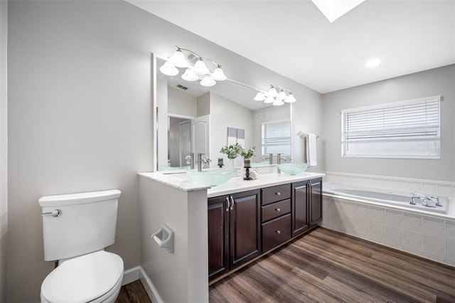 bathroom featuring an inviting chandelier, wood-type flooring, toilet, vanity, and tiled tub