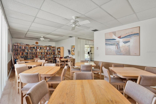 dining area featuring ceiling fan, light hardwood / wood-style flooring, and a drop ceiling