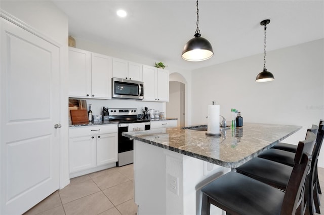 kitchen featuring decorative light fixtures, stainless steel appliances, dark stone counters, and an island with sink