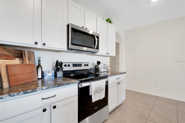 kitchen with white cabinets, light tile patterned floors, stainless steel appliances, and dark stone countertops