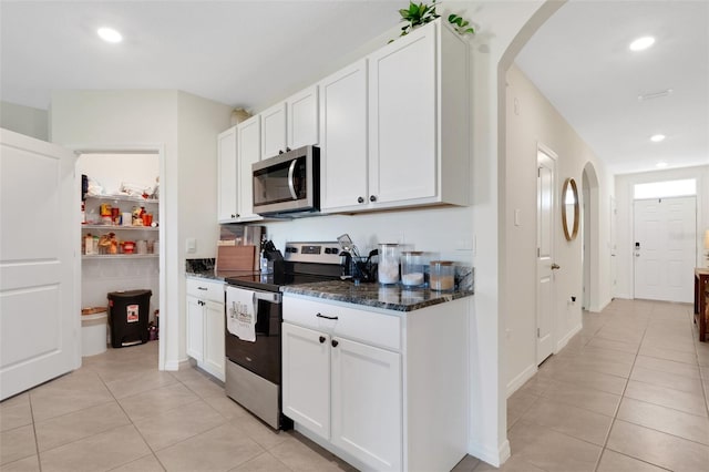 kitchen featuring white cabinets, light tile patterned floors, stainless steel appliances, and dark stone counters