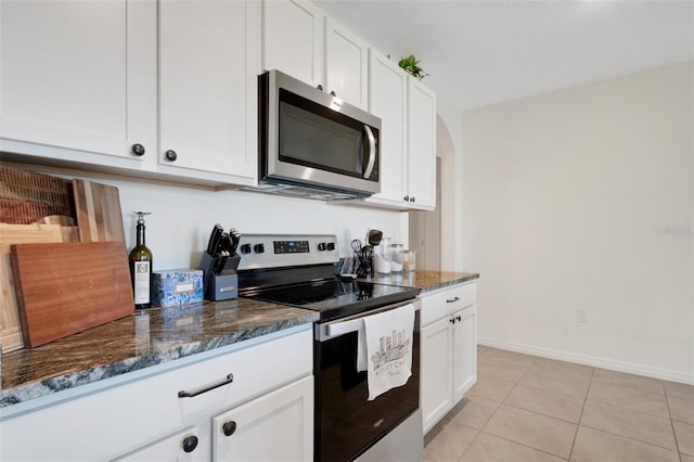 kitchen with white cabinets, light tile patterned floors, appliances with stainless steel finishes, and dark stone counters