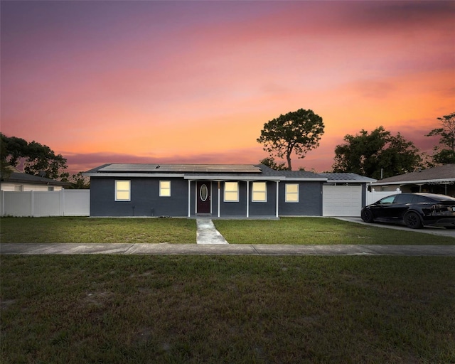 ranch-style house featuring aphalt driveway, a lawn, fence, solar panels, and a garage