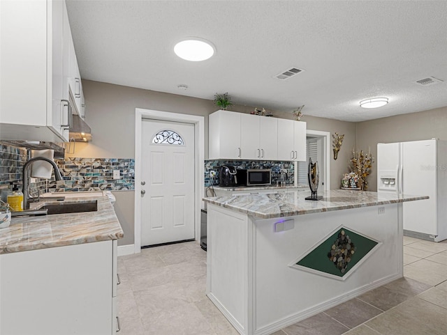 kitchen with decorative backsplash, a sink, white fridge with ice dispenser, and visible vents