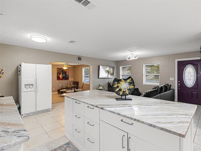 kitchen with white fridge with ice dispenser, a ceiling fan, white cabinets, visible vents, and light tile patterned flooring