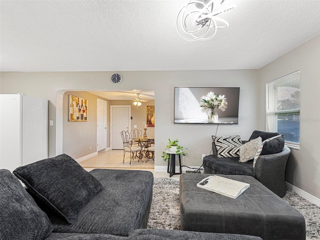 living room featuring arched walkways, baseboards, ceiling fan, and a textured ceiling