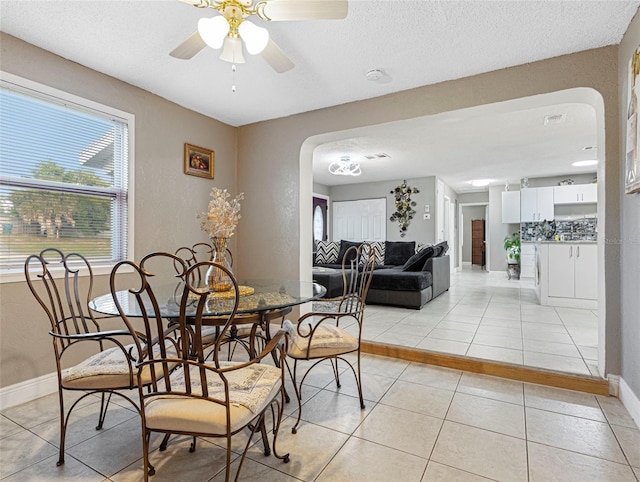 dining space featuring arched walkways, light tile patterned flooring, baseboards, and a ceiling fan