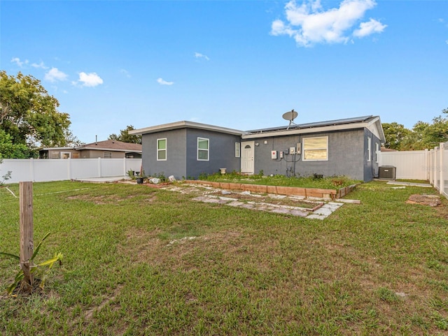 back of house with a fenced backyard, roof mounted solar panels, a lawn, and central air condition unit