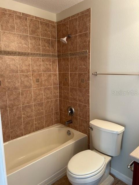 full bathroom with tiled shower / bath combo, vanity, a textured ceiling, and toilet