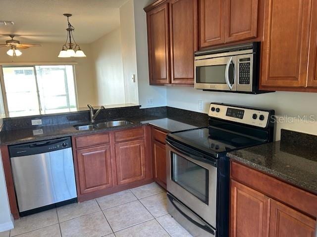 kitchen featuring sink, light tile patterned floors, stainless steel appliances, decorative light fixtures, and dark stone counters