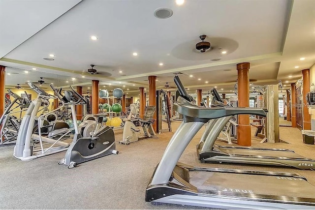 gym with a tray ceiling, ornate columns, ceiling fan, and light colored carpet