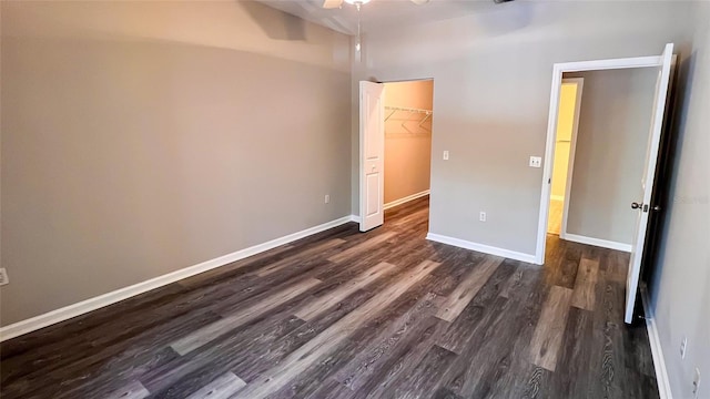 unfurnished bedroom featuring a closet, ceiling fan, dark hardwood / wood-style flooring, and a walk in closet