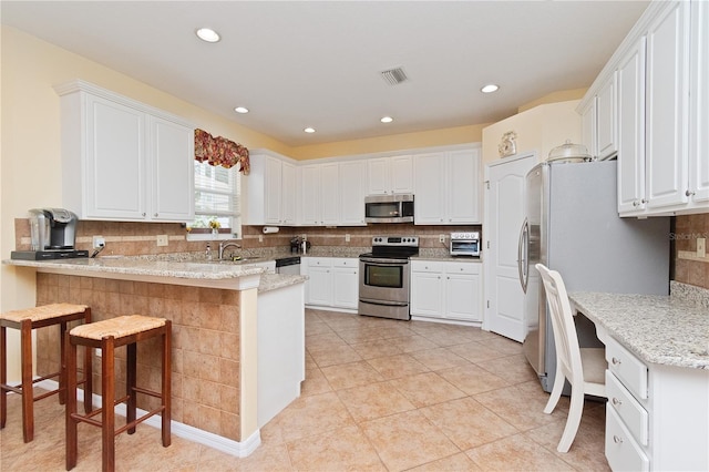 kitchen with appliances with stainless steel finishes, tasteful backsplash, white cabinetry, a kitchen bar, and kitchen peninsula