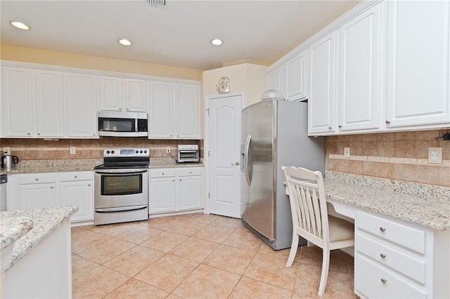 kitchen featuring stainless steel appliances, tasteful backsplash, built in desk, white cabinets, and light tile patterned flooring