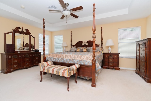 bedroom with a raised ceiling, light colored carpet, and ceiling fan