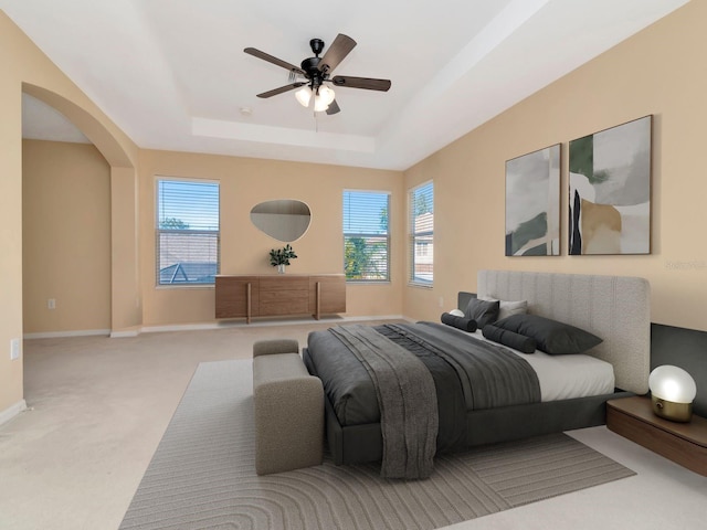 bedroom with a raised ceiling, ceiling fan, light carpet, and multiple windows